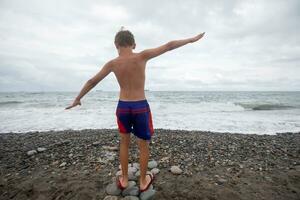 de jongen wandelingen langs de rotsachtig kust van de zee.recreatie Bij de zee Aan zomer vakantie. foto