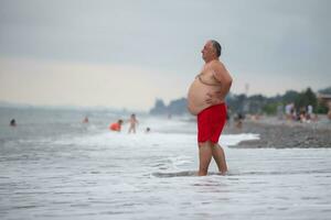 een te zwaar ouderen Mens is resting Aan de zee. foto