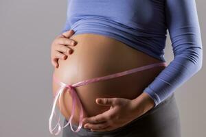 beeld van maag van zwanger vrouw met een roze lint Aan grijs achtergrond. foto
