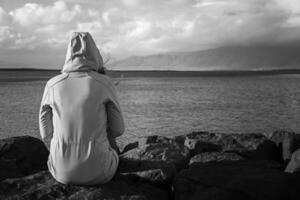 zwart en wit beeld van vrouw zittend Bij de kustlijn in reykjavik en op zoek Bij de zee.afbeelding bevat weinig lawaai omdat van hoog iso. foto