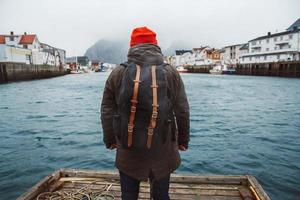 man die op de houten pier staat op de achtergrond van de vissershuizen, de bergen en het meer foto