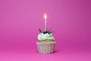 verjaardag koekje met een brandend kaarsen over- roze achtergrond foto