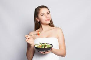 mooi brunette meisje in handdoek aan het eten vers salade en glimlachen foto