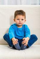 schattig weinig jongen is zittend Aan bank. foto