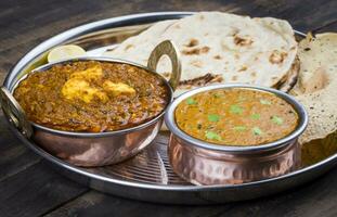 Indisch traditioneel thali voedsel dal makhani geserveerd met chapati, papa, kadai paneer of citroen Aan wijnoogst houten achtergrond foto