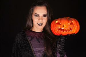 dame in heks kostuum Holding een pompoen over- zwart achtergrond voor halloween. foto