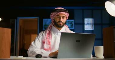 Arabisch werknemer concentreren Aan afwerking omhoog belangrijk baan taken, van een afstand werken van elegant appartement persoonlijk kantoor. gefocust moslim telewerker typen Aan laptop toetsenbord foto