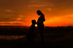 silhouetten van man zoenen maag van zijn zwanger vrouw terwijl ze genieten uitgeven tijd samen buiten.afgezwakt afbeelding. foto