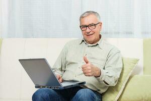 senior Mens tonen duim omhoog terwijl gebruik makend van laptop. foto