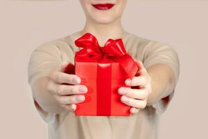 bijgesneden vrouw shows een geschenk met een rood boog. ze Holding een geschenk in haar handen en lachend. dichtbij omhoog naakt foto