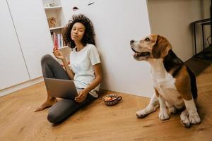 zwarte jonge vrouw die laptop gebruikt en haar hond aait foto