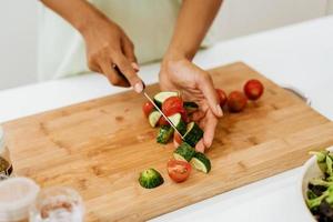 zwarte jonge vrouw die salade maakt tijdens het koken van de lunch in de keuken foto