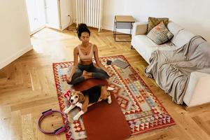 zwarte jonge vrouw die mediteert tijdens yogapraktijk met haar hond