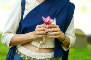 detailopname handen van een mooi Thais jong dame ware Thais noordelijk traditioneel jurk Holding roze bloem Aan wazig achtergrond. foto