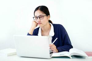 detailopname Aziatisch jong vrouw leerling in gewoontjes kleding shows verveling in aan het doen rapporten of huiswerk met laptop Aan wit helling achtergrond. Aziatisch school- concept. foto