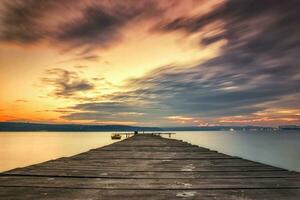 spannend lucht met wolken Bij de kust met houten pier en boot foto