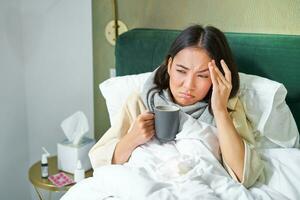 griep, ziekte en mensen. jong vrouw gevoel ziek, hebben koorts en vangen col, aan het liegen in bed met heet thee, nemen verdovende middelen van influenza foto