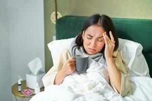 griep, ziekte en mensen. jong vrouw gevoel ziek, hebben koorts en vangen col, aan het liegen in bed met heet thee, nemen verdovende middelen van influenza foto