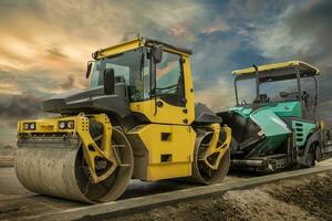 trommel rol en asfalt verspreiden machine. weg bouw. toepassen nieuw heet asfalt gebruik makend van weg bouw machinerie en macht industrieel hulpmiddelen. foto