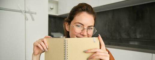 dichtbij omhoog portret van jong vrouw lachend, Holding notitieboekje, tonen haar ontwerper foto