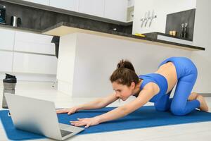 beeld van jong sportvrouw, geschiktheid meisje aan het kijken online yoga zelfstudie Aan laptop en sporten, in aansluiting op video instructies foto