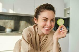 portret van Vrolijk, glimlachen jong vrouw in de keuken, Koken, hakken courgette, Holding groenten en op zoek Vrolijk, voorbereidingen treffen veganistisch voedsel maaltijd Bij huis foto