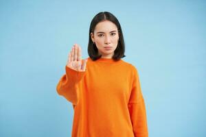 hou op. echt en zelfverzekerd Koreaans vrouw model, strekt zich uit hand, shows taboe, afwijzing gebaar, weigeren iets, staat over- blauw achtergrond foto