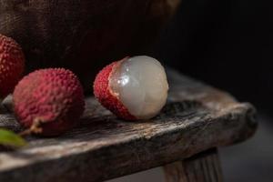 lychee wordt in een houten bord geplaatst, geschild of ongeopend, op een donkere houtnerftafel foto