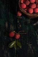 lychee wordt in een houten bord geplaatst, geschild of ongeopend, op een donkere houtnerftafel
