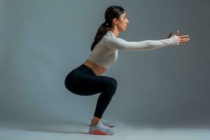 vrouw aan het doen squats met uitgestrekt handen Aan grijs achtergrond foto