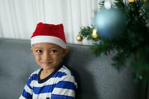 vrolijk Kerstmis 2024 concept Aziatisch jongen siert Kerstmis boom met kleurrijk Kerstmis ballen. foto