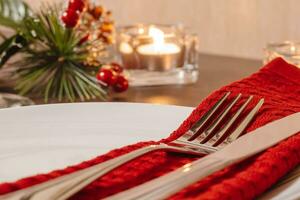 Kerstmis tafel instelling. bord en bestek Aan servet. voorbereidingen treffen voor feestelijk diner. kaarsen brandend Aan tafel Aan Kerstmis vooravond. foto
