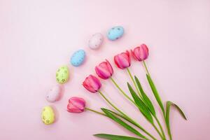 geschilderd eieren met tulpen Aan roze achtergrond. Pasen, de lente. pastel achtergrond. vlak leggen. kopiëren ruimte foto