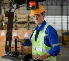 Mens arbeider Bij heftruck bestuurder gelukkig werken in industrie fabriek logistiek schip. Mens heftruck bestuurder in magazijn Oppervlakte. heftruck bestuurder zittend in voertuig in magazijn foto