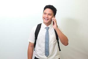 Indonesisch senior hoog school- leerling vervelend wit overhemd uniform met grijs stropdas op zoek omhoog terwijl hebben gesprek Aan telefoon telefoongesprek. geïsoleerd beeld Aan wit achtergrond foto