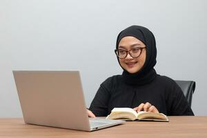 portret van aantrekkelijk Aziatisch hijab vrouw werken Aan haar laptop. moslim meisje lezing een boek in kantoor. werknemer en freelance arbeider concept. foto