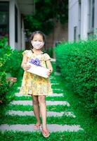 kleintje Aziatisch meisje vervelend masker in geel jurk Holding Cadeau doos in haar verjaardag in de park foto