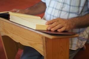 moslim Mens hand- Holding heilig boek koran Bij moskee foto