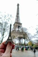 een persoon Holding een miniatuur eiffel toren in voorkant van de eiffel toren foto