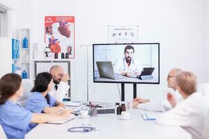 medisch personeel pratend met deskundige dokter gedurende webinar in ziekenhuis conferentie kamer. geneeskunde personeel gebruik makend van internet gedurende online vergadering met deskundige dokter voor expertise. foto