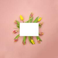 voorjaar bloem arrangement Aan een gekleurde achtergrond. roze en geel tulpen met een blanco kaart Aan een roze achtergrond. foto