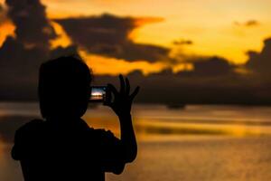 silhouetten mensen het schieten de zonsondergang Bij de meer. foto