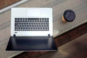 mockup beeld van laptop met blanco zwart scherm en koffie kop Aan metaal bank in natuur buitenshuis park foto