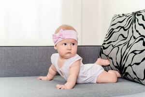 portret van een baby meisje met een verband en een boog Aan haar hoofd Aan een sofa foto