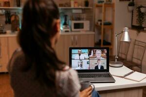 zakenvrouw hebben een video conferentie met team gedurende middernacht gebruik makend van laptop in huis keuken. zakelijke vergadering gebruik makend van modern technologie, laptop laat Bij nacht , techniek, bureau, adviseur, werk, discussie. foto