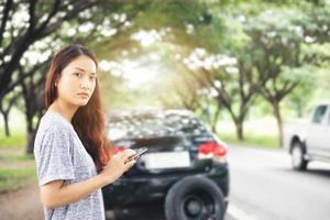 Aziatische vrouw die mobiele telefoon gebruikt terwijl ze kijkt en gestresste man zit na een autopech op straat