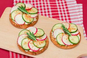 licht ontbijt of eetpatroon aan het eten krokant kraker belegd broodje met room kaas, vers komkommer en radijs Aan houten Koken bord Aan magenta achtergrond foto