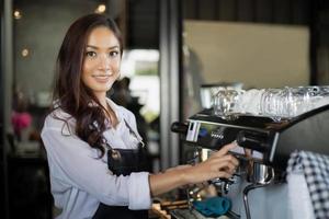 aziatische vrouwenbarista glimlacht en gebruikt koffiemachine in coffeeshopteller - werkende vrouw, eigenaar van een klein bedrijf, eten en drinken caféconcept foto