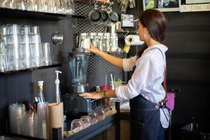 aziatische vrouwenbarista glimlacht en gebruikt koffiemachine in coffeeshopteller - werkende vrouw, eigenaar van een klein bedrijf, eten en drinken caféconcept foto