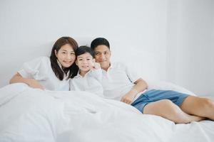 gelukkige Aziatische familie met zoon thuis op de slaapkamer die speelt en lacht foto
